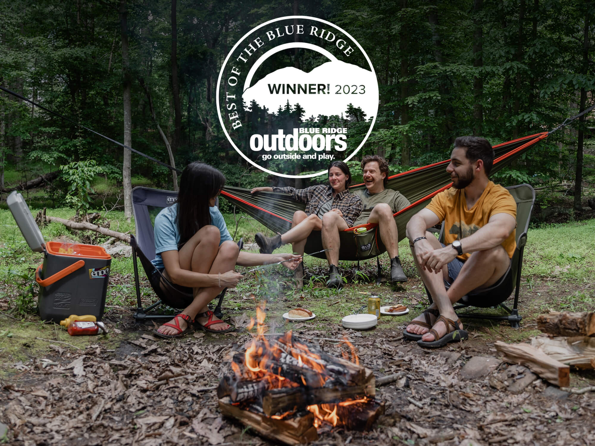Friends relaxing outside in portable camp chairs and ENO DoubleNest hammock near campfire. Best of the Blue Ridge Award logo is visible.