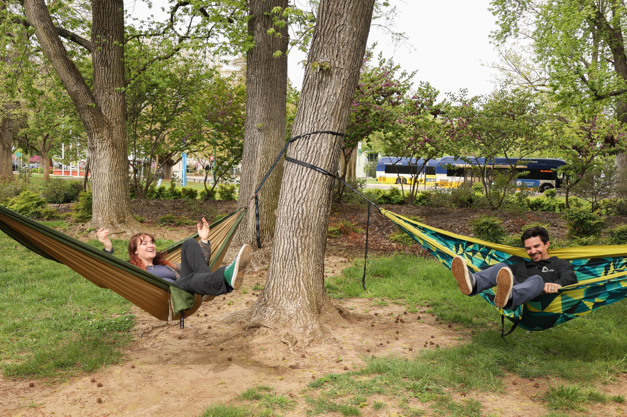 Two people hammocking in an ENO Hammocks separate hammocks with the city and busses in the background