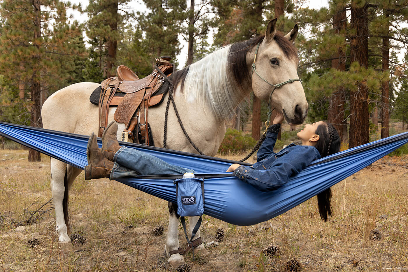 A woman lays in her ENO hammock while petting a horse