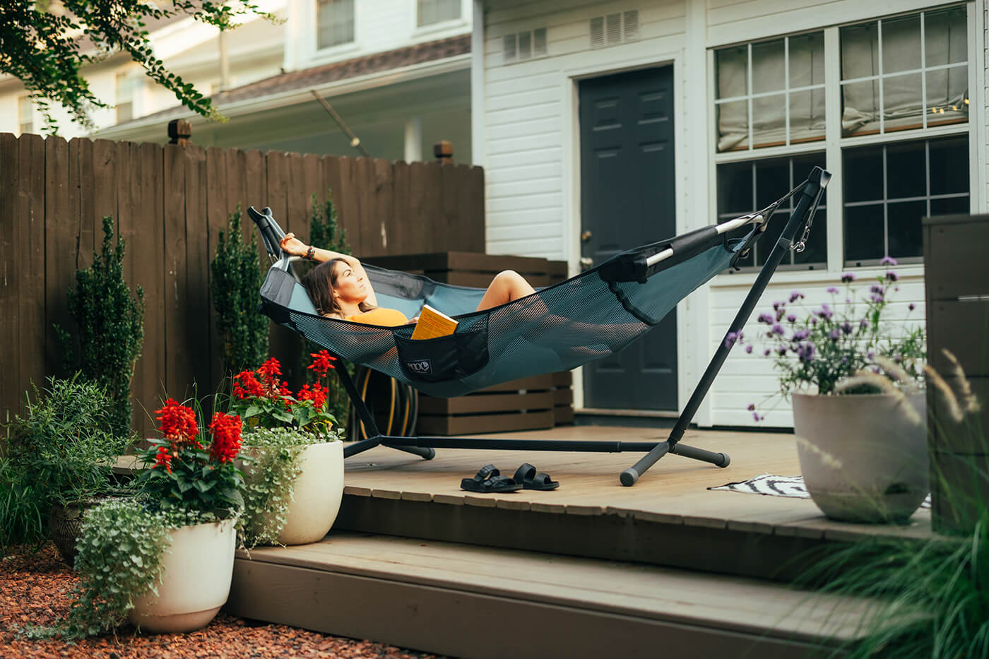 A person lays in the ENO DayLoft Hammock while on their back porch surrounded by plants.