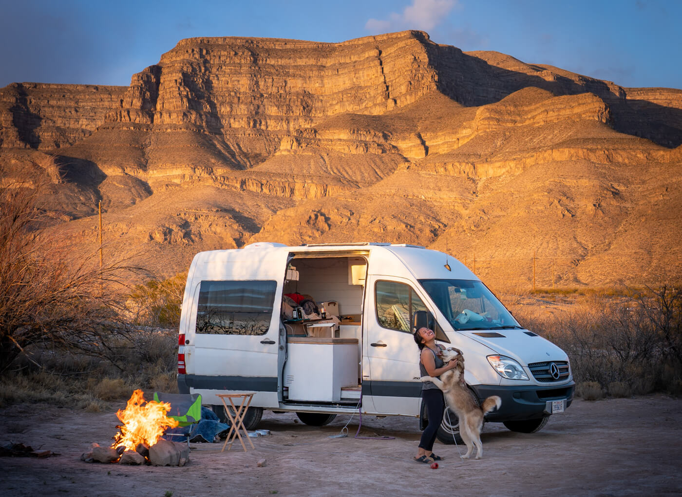 A dog jumping on Kay near her van and a campfire with some canyons in the background
