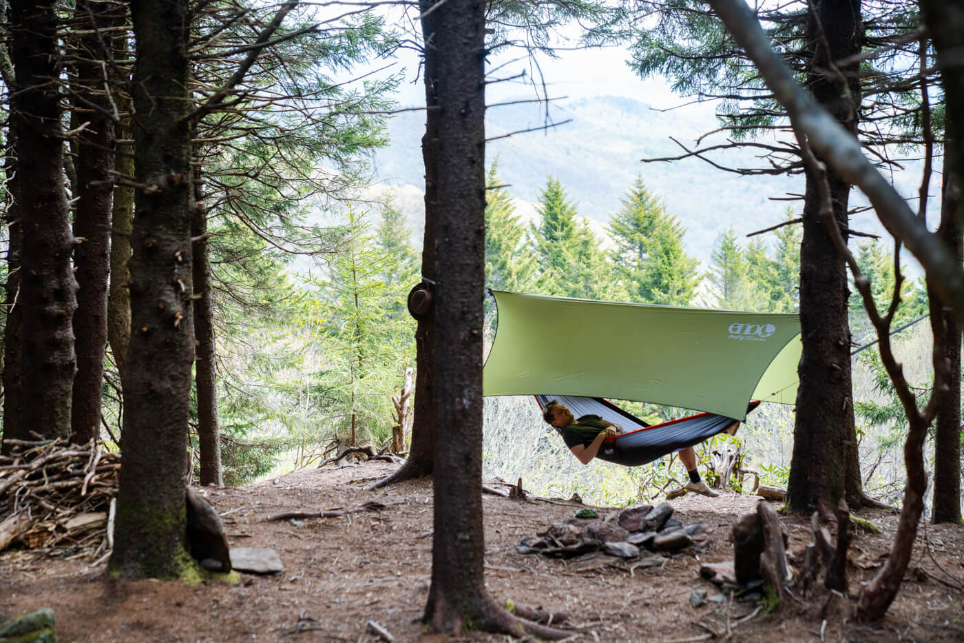 A person in an ENO hammock with an ENO tarp overhead. The person is in the woods
