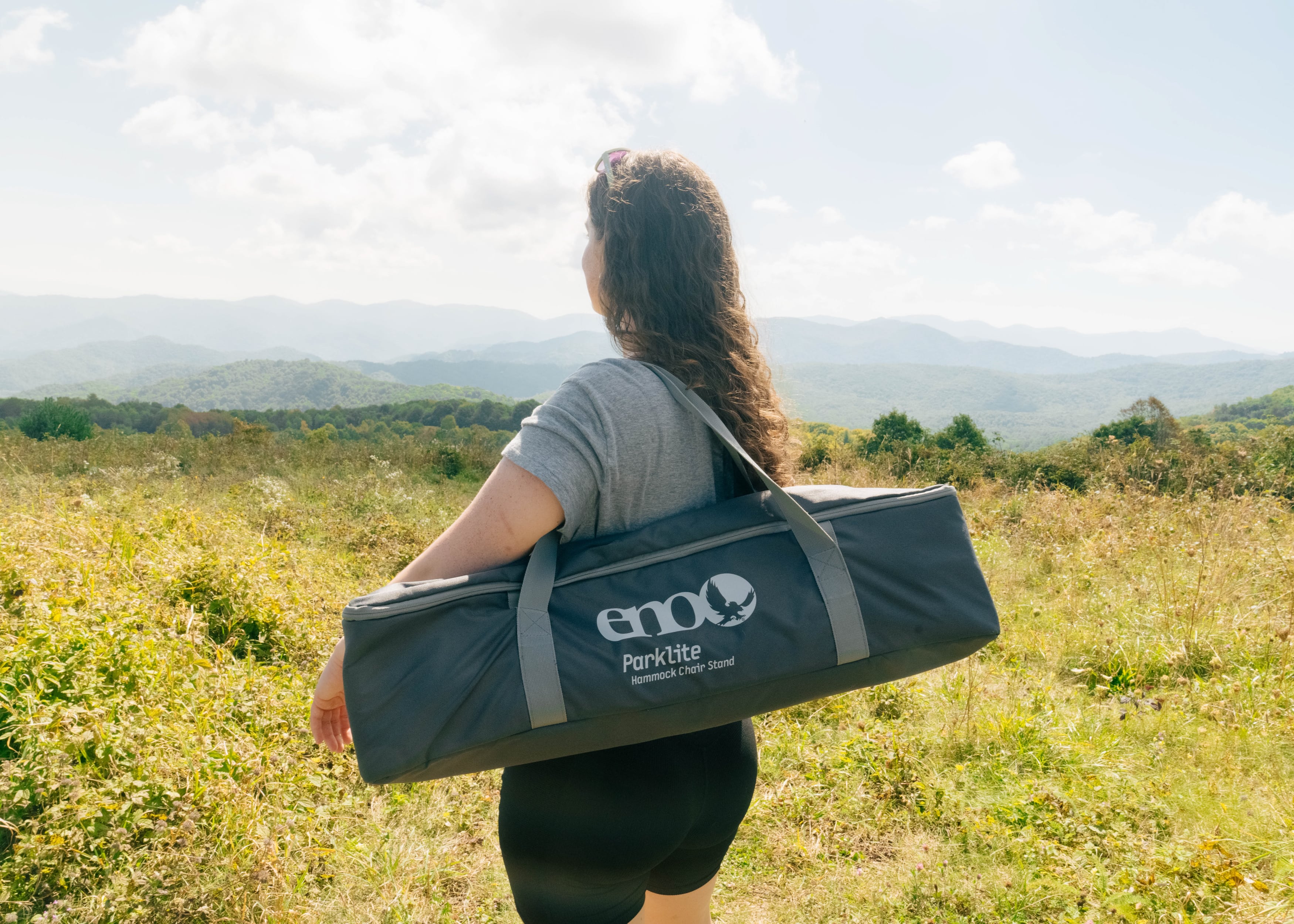 A woman looking at mountain ranges at Max Patch. She is holding a packed up ENO Parklite Hammock Chair Stand