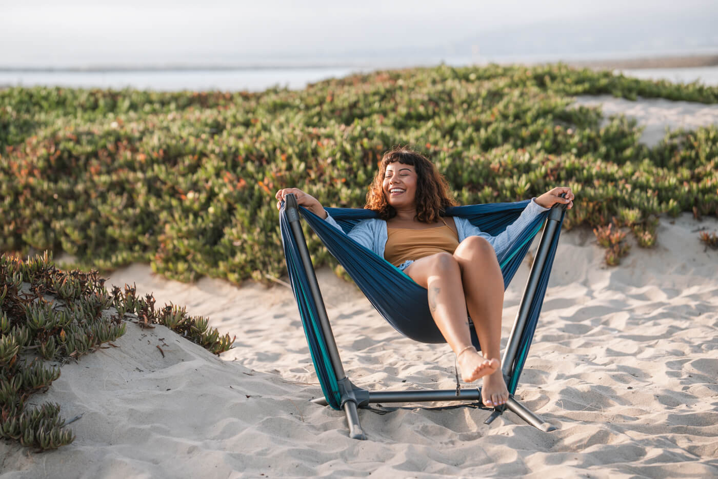 A woman sits in her ENO Parklite Hammock Chair Stand on the beach