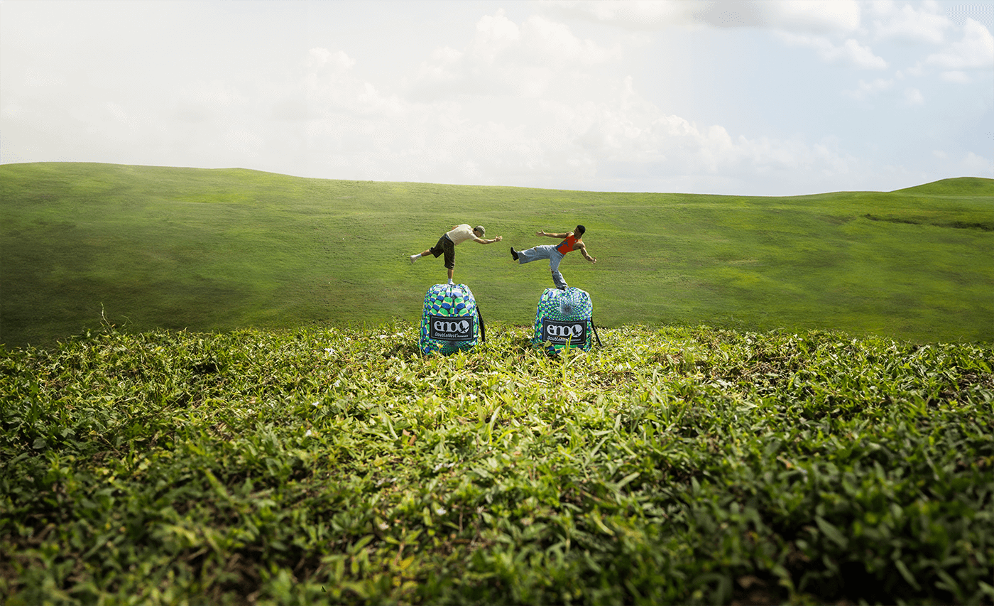 An optical illusion of two people balancing on two packed up ENO Optical Illusion DoubleNest Hammocks in a field
