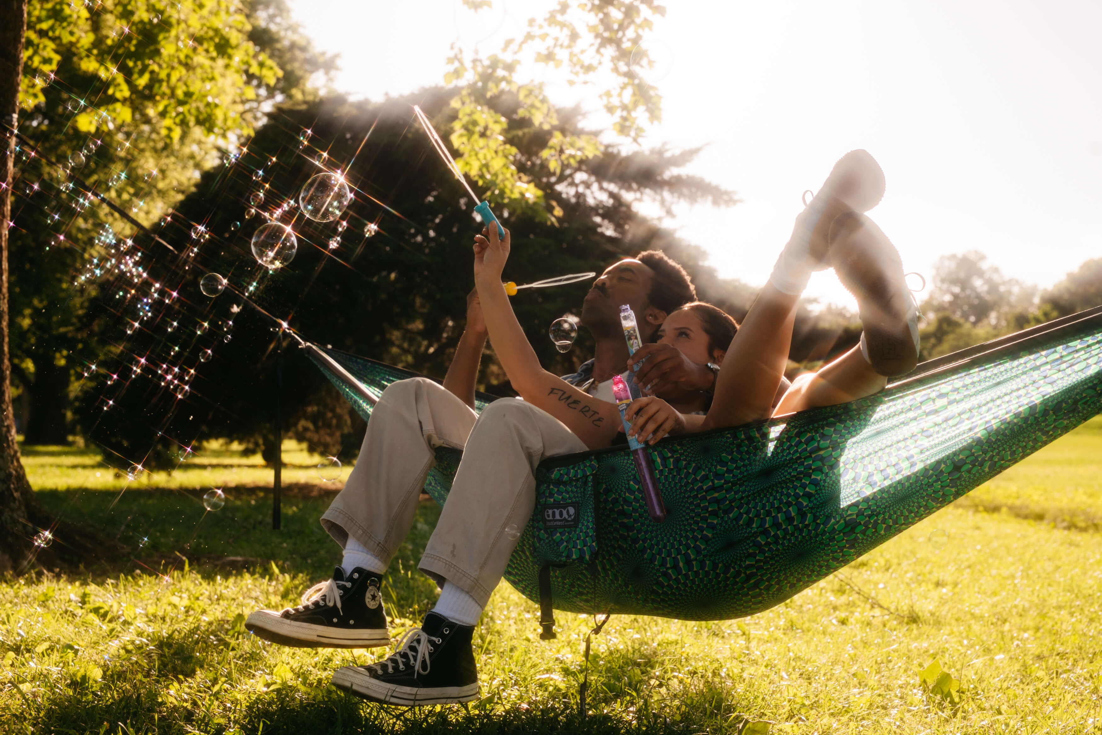 A man and woman in an ENO DoubleNest Hammock while blowing bubbles