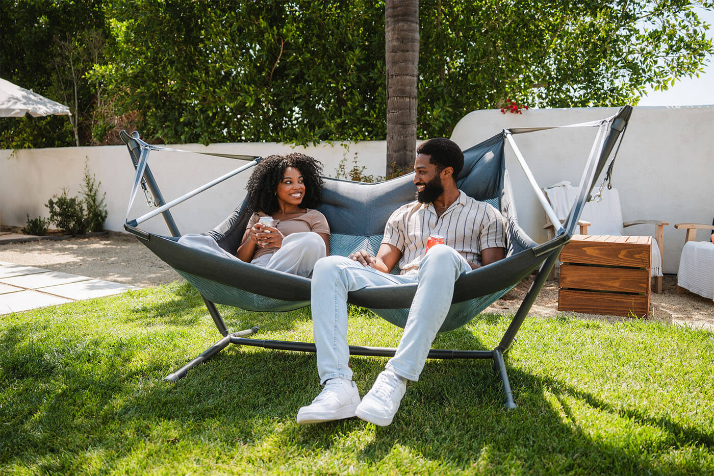 A man and woman laugh together while sitting in the ENO DoubleLoft Chair in their backyard.