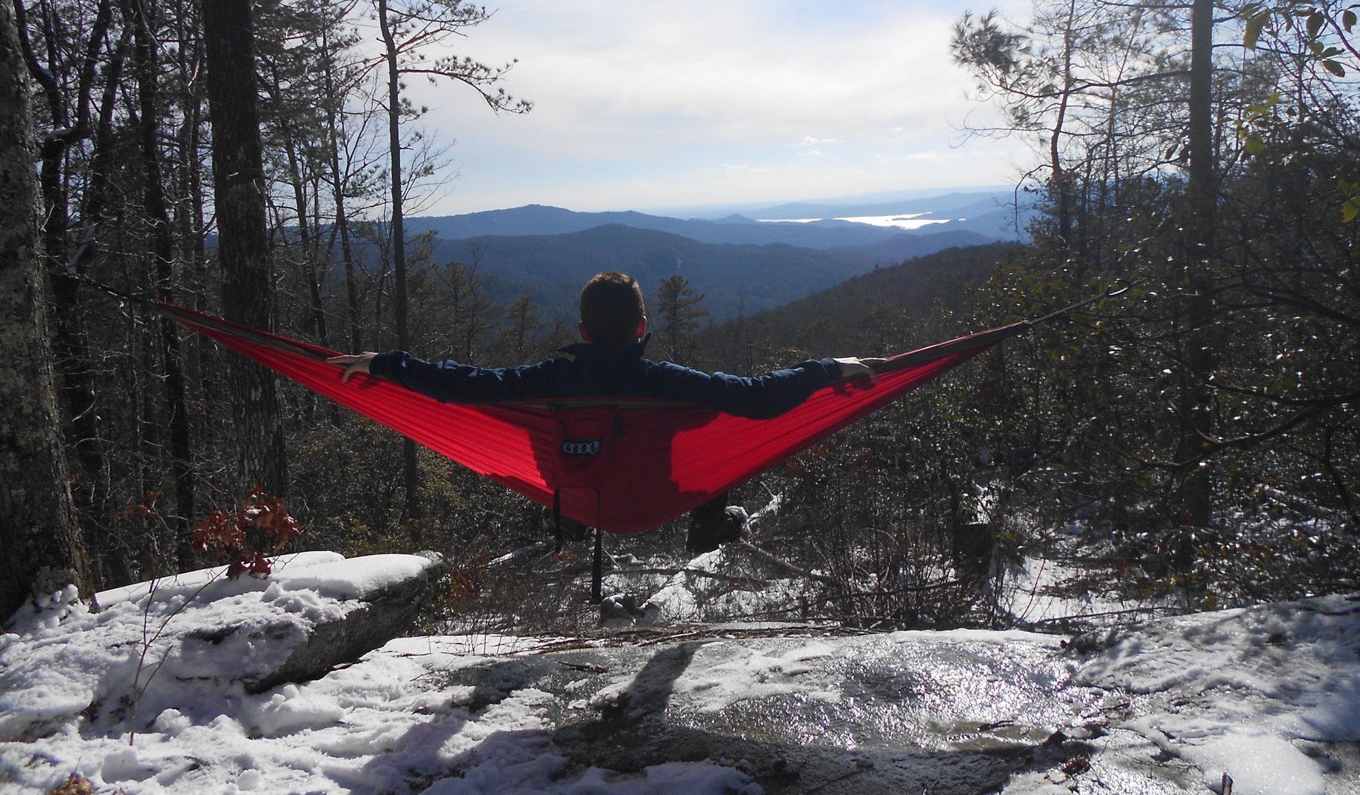 Man hanging in a red ENO hammock over snow covered ground