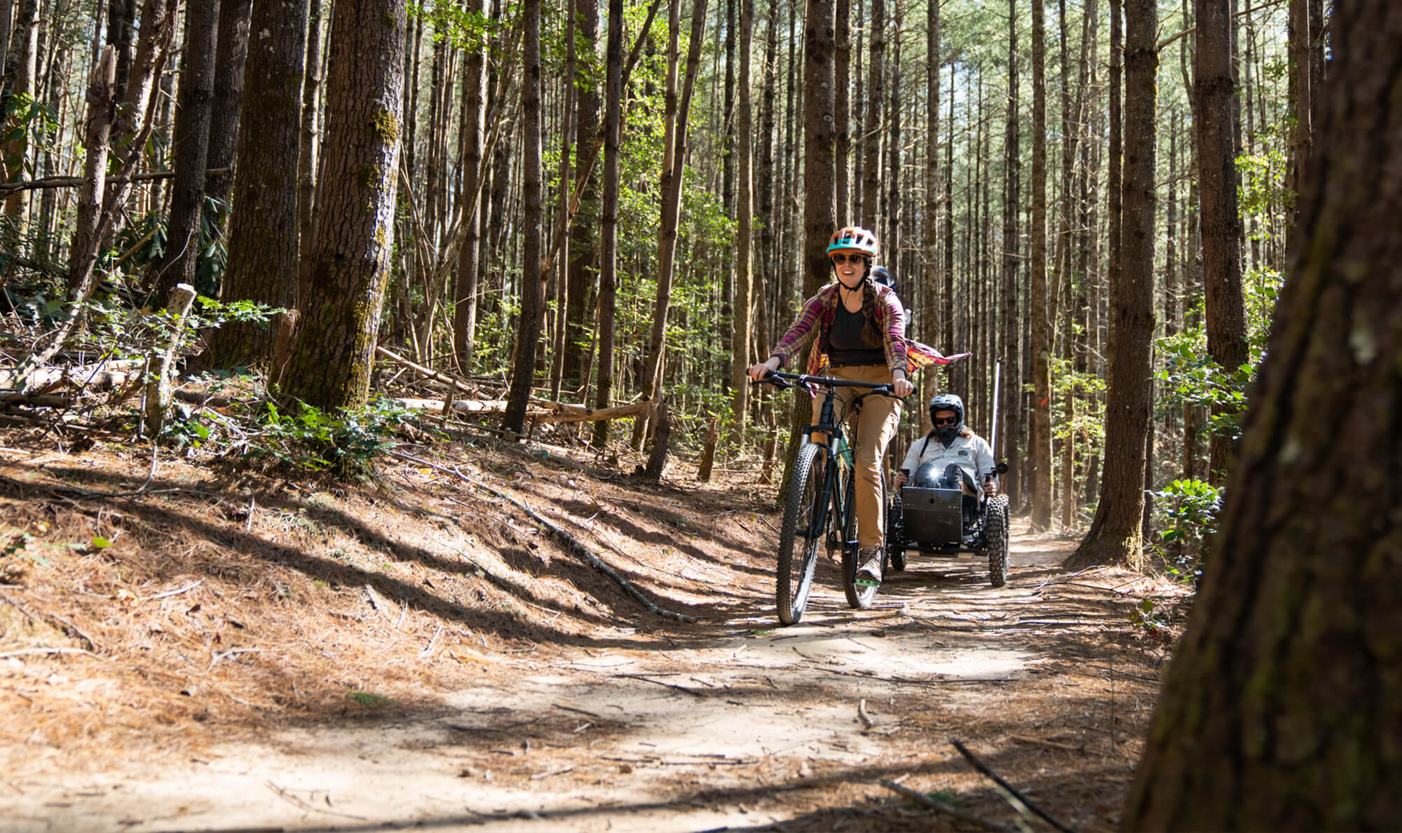 Anna Belle, rides a mountain bike, and Thomas rides the Outrider Coyote through a forest of pine trees.