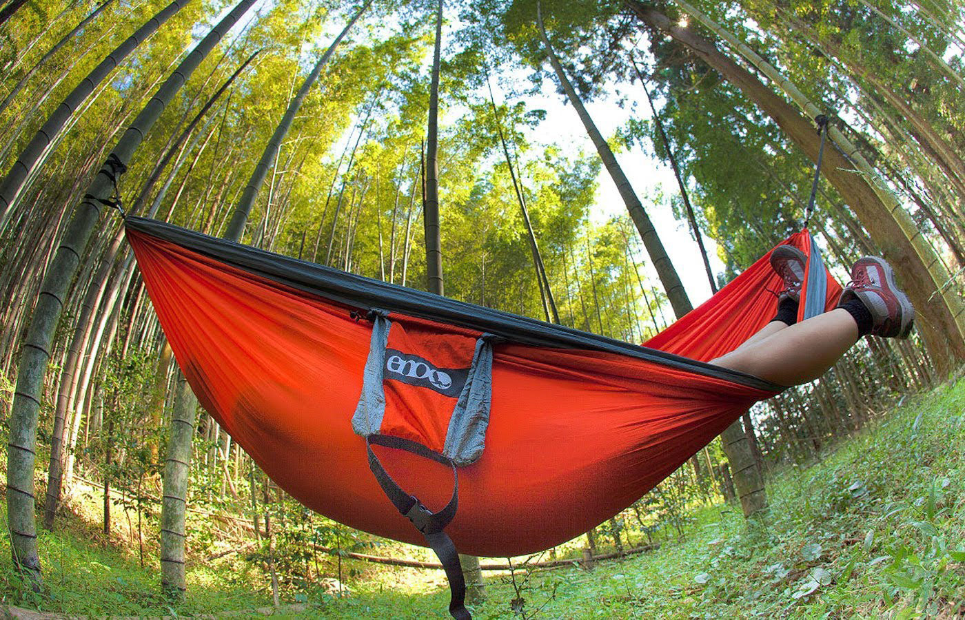 A fish-eye type photo of someone laying in an ENO hammock with trees in the background
