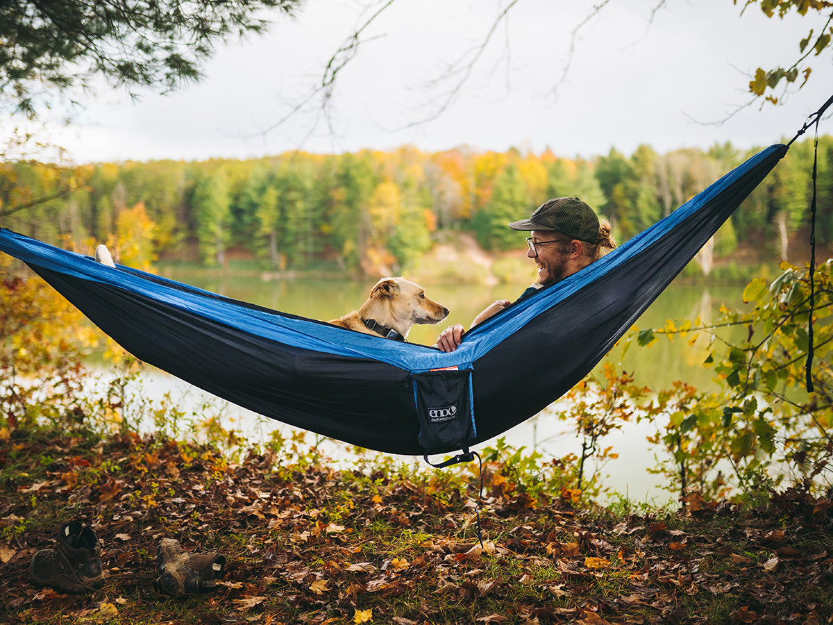 Man and dog inside an ENO hammock together near trees and lake