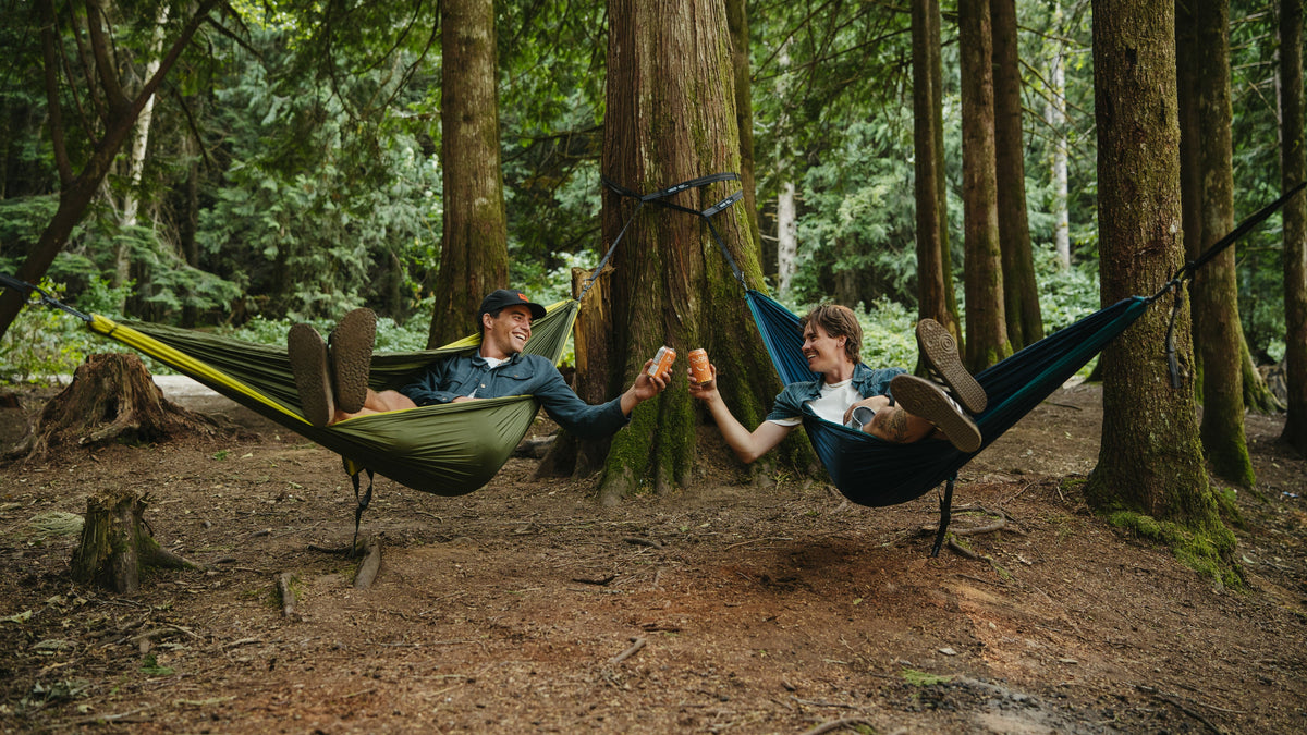 Two men in separate hammocks cheers their cans
