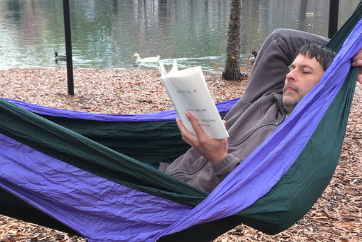 A man reads in an ENO hammock by a pond