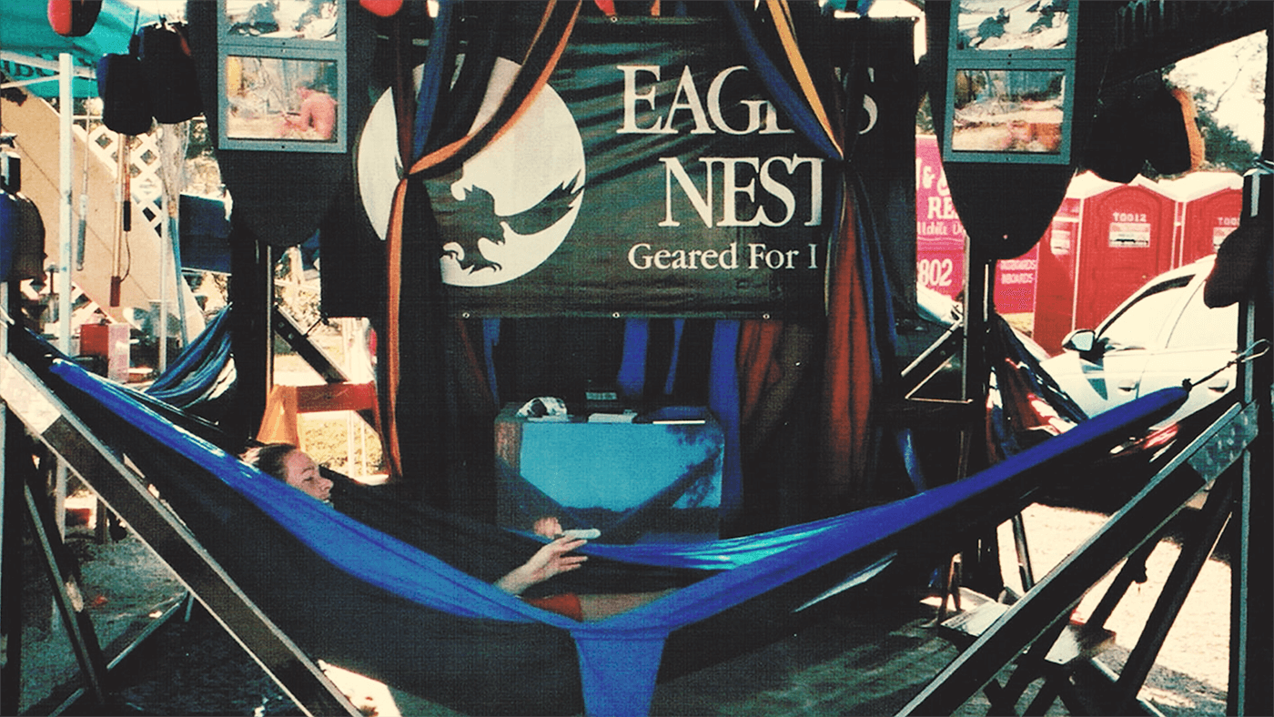 A person in an ENO hammock in an ENO hammock stand with an ENO banner behind them at a booth