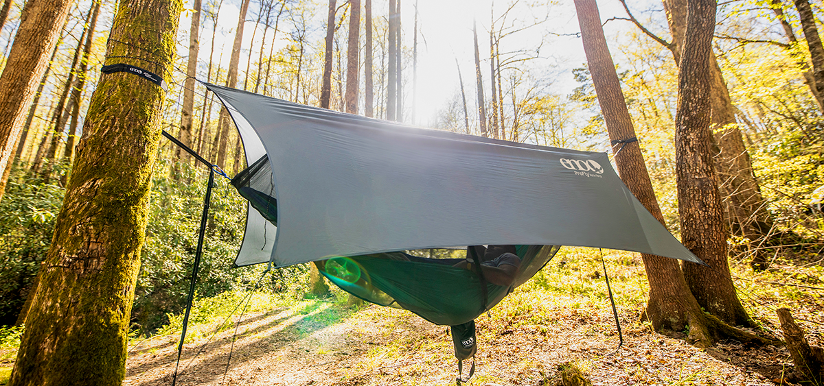 A gray ENO tarp hanging over an ENO hammock in the woods