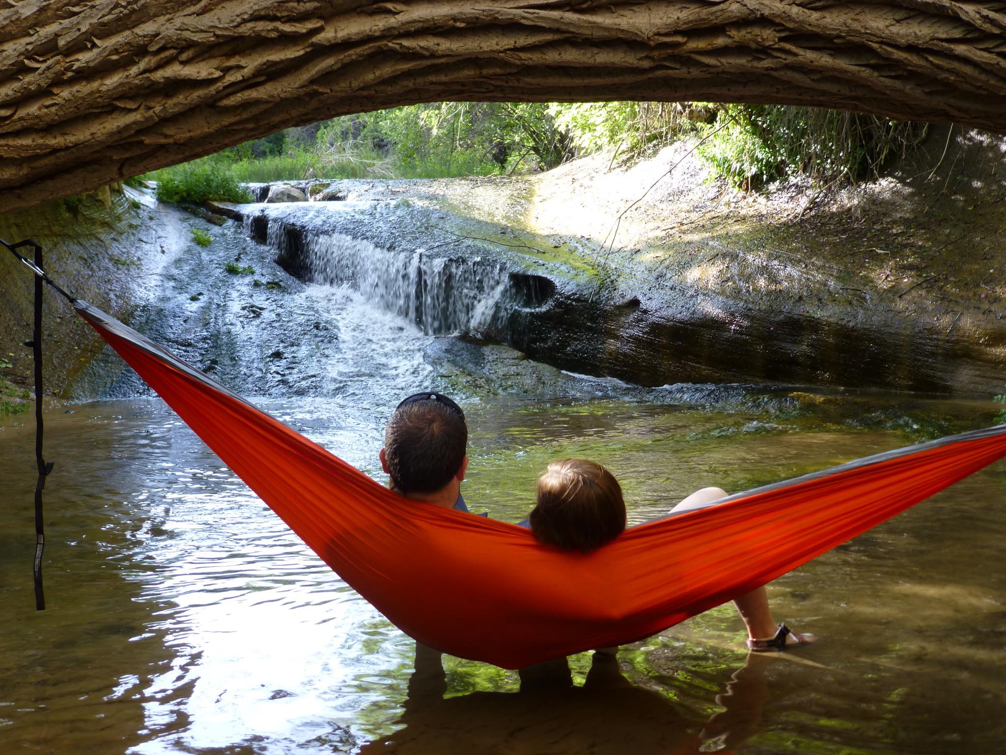 Two people hammocking in an ENO Hammock over a shallow creek while looking at a small waterfall