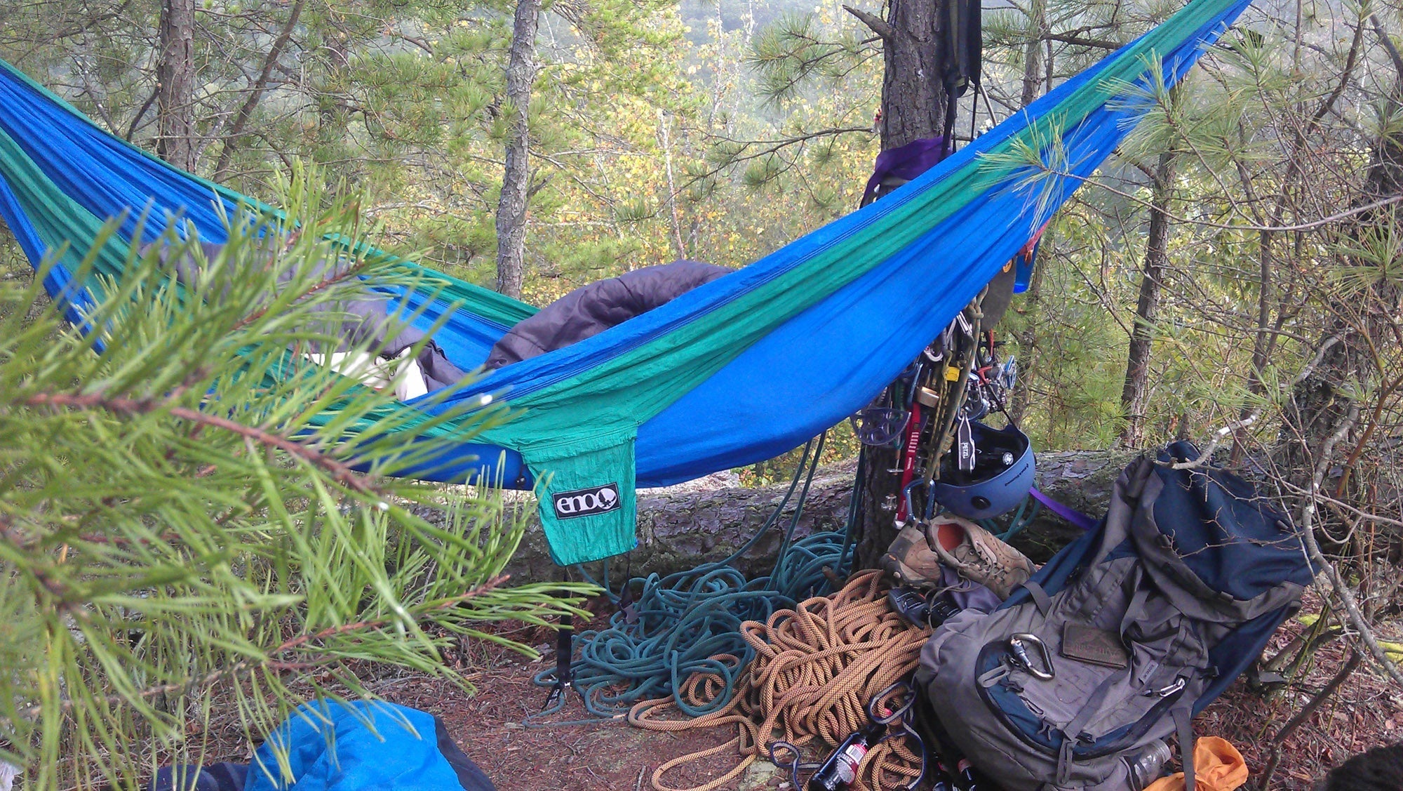 An ENO hammock strung between trees with various ropes and backpacks around it