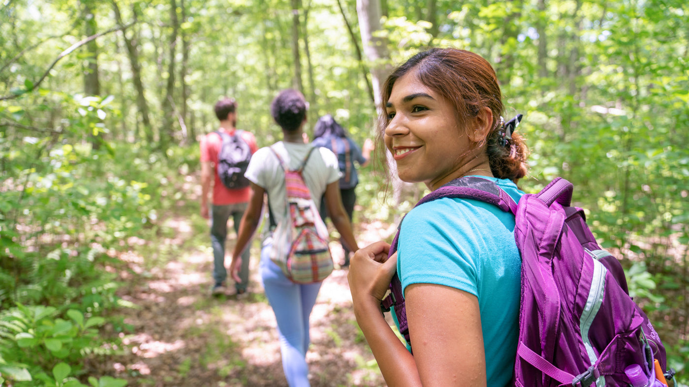 A woman smiles while hiking in a dense forest with a group of three other people.