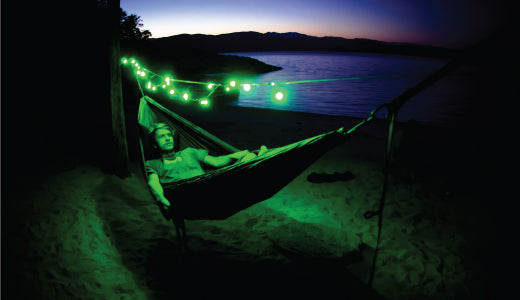 Man hanging in his hammock at night with green LED string lights hanging over him