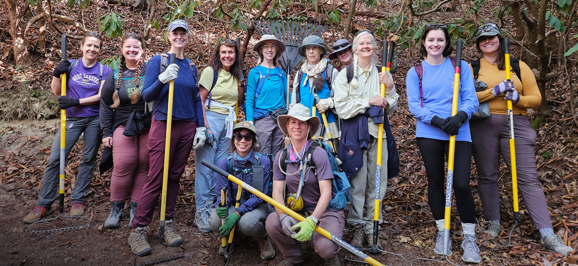 Group of people with tools posing for a photo in a forest setting