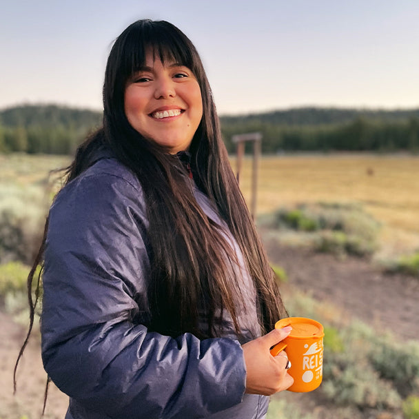 Cindy Villasenor, a young woman with long black hair and bangs, wears a winter jacket as she smiles at the camera while holding a coffee cup outside.