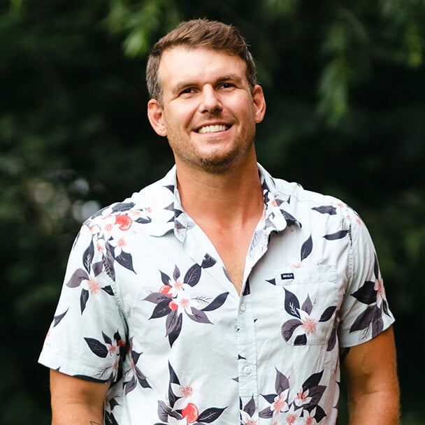 Ryan Tipton, a professional lifestyle photographer, smiles at the camera while wearing a collared shirt with flowers.