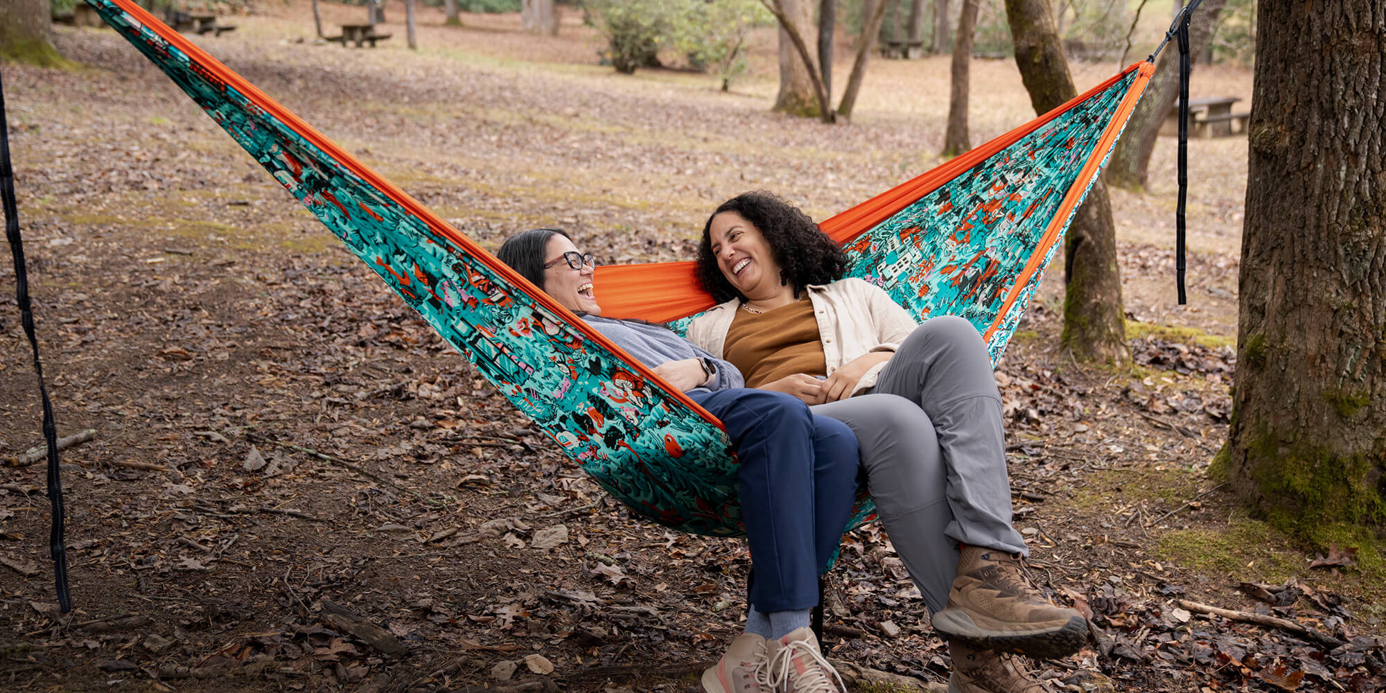Two people sitting in an ENO Giving Back hammock in a forest setting