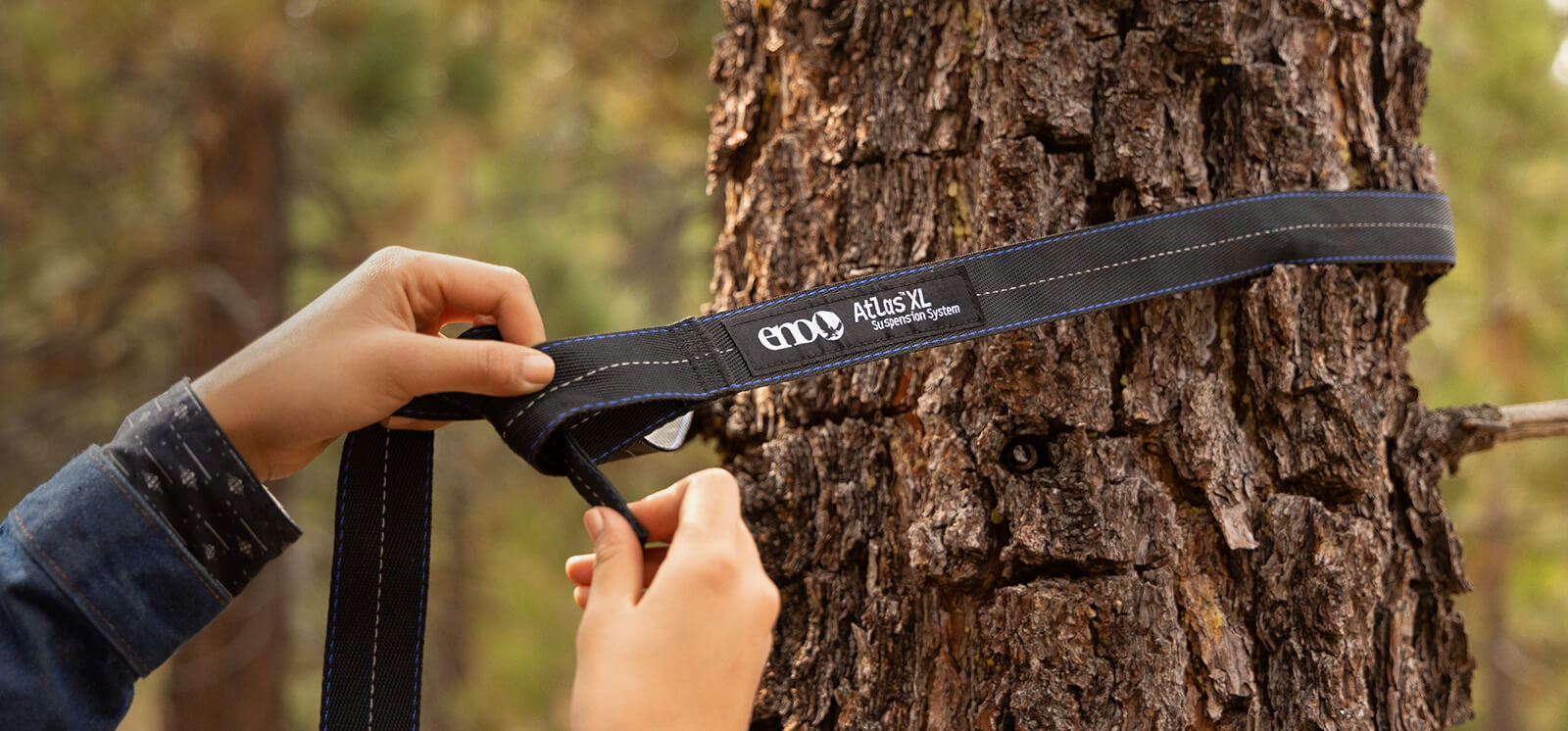 Person securing the Atlas XL Hammock Straps to a tree in a forest setting