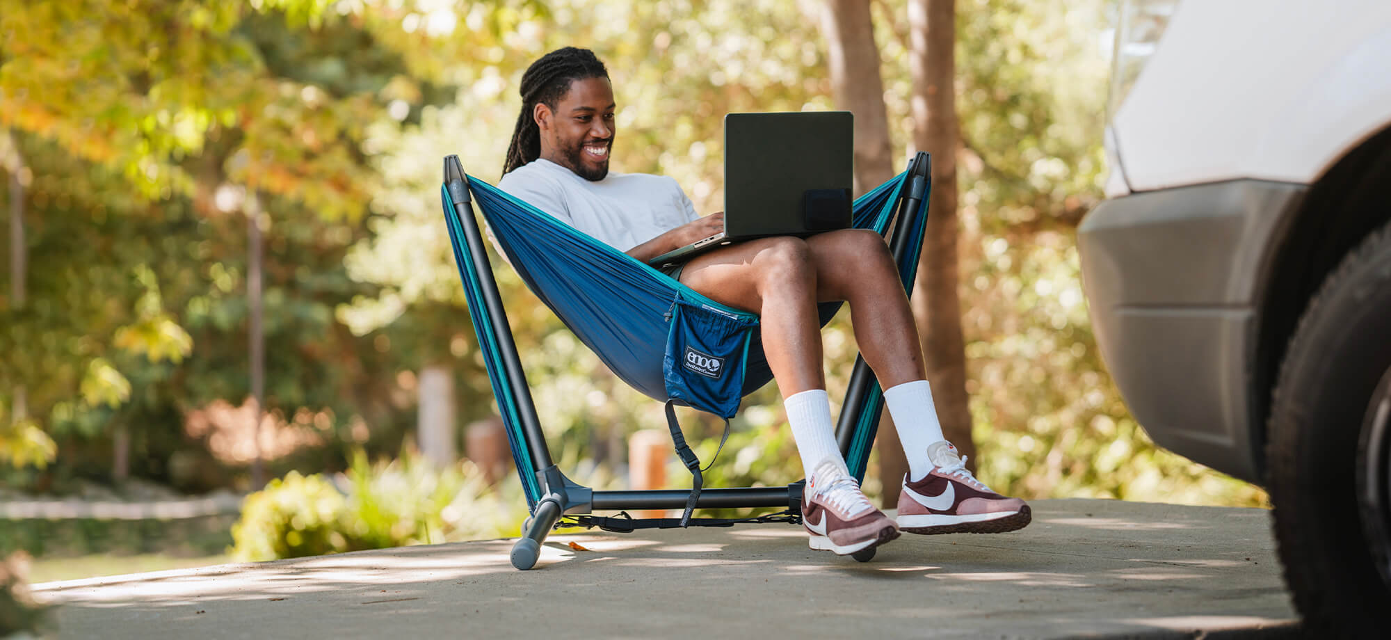 Young man sits in ENO hammock set up on the Parklite Hammock Chair Stand with a laptop in his lap.