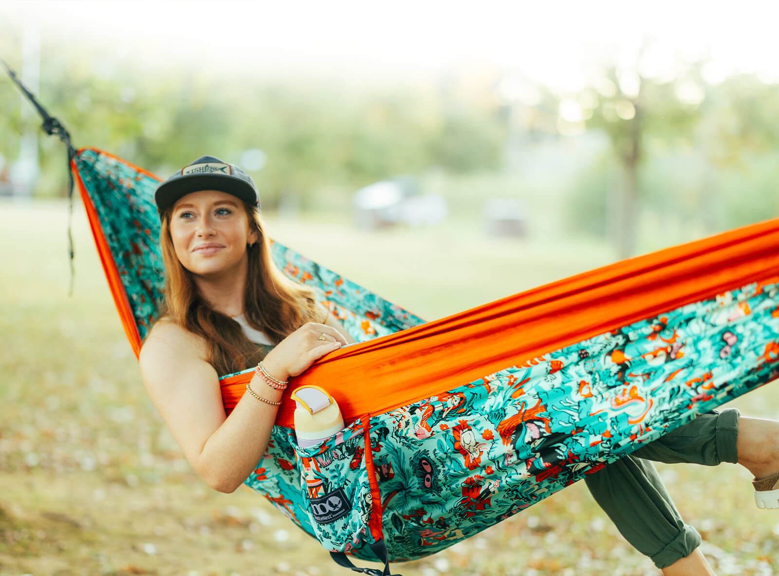 Person sitting in an ENO In Good Company Giving Back Hammock with a patterned design in an outdoor setting.