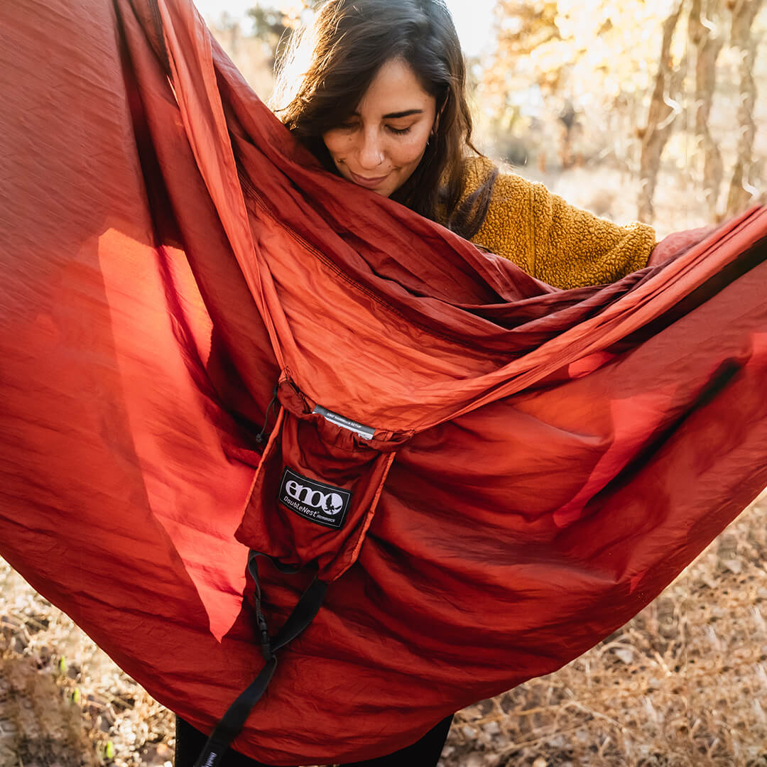Woman holding an unpacked ENO DoubleNest Hammock in Canyon Coral while looking down at woven label.