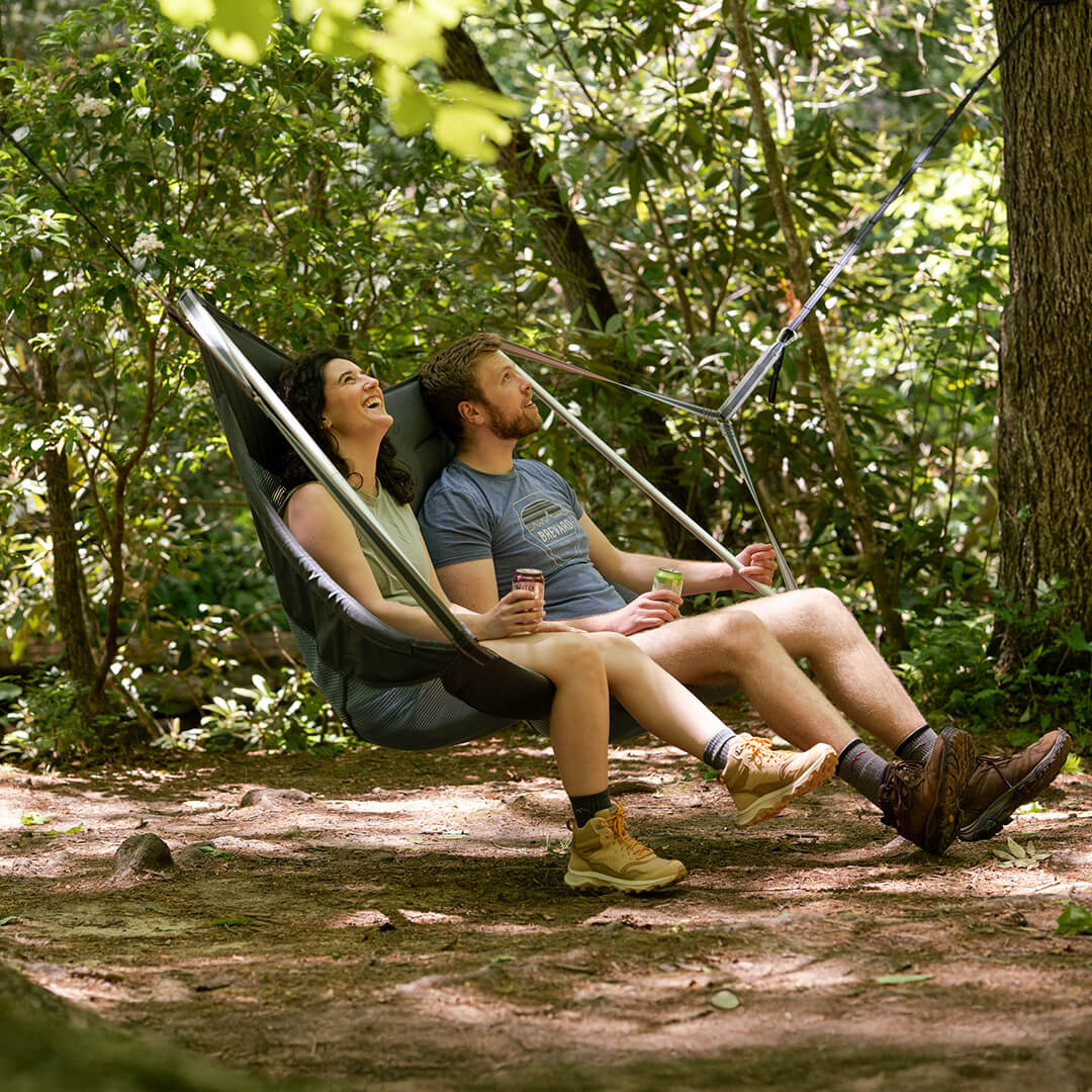 Two people sitting in an ENO DoubleLoft Hammock Chair connected to ENO Atlas Hammock Straps in a forest setting.