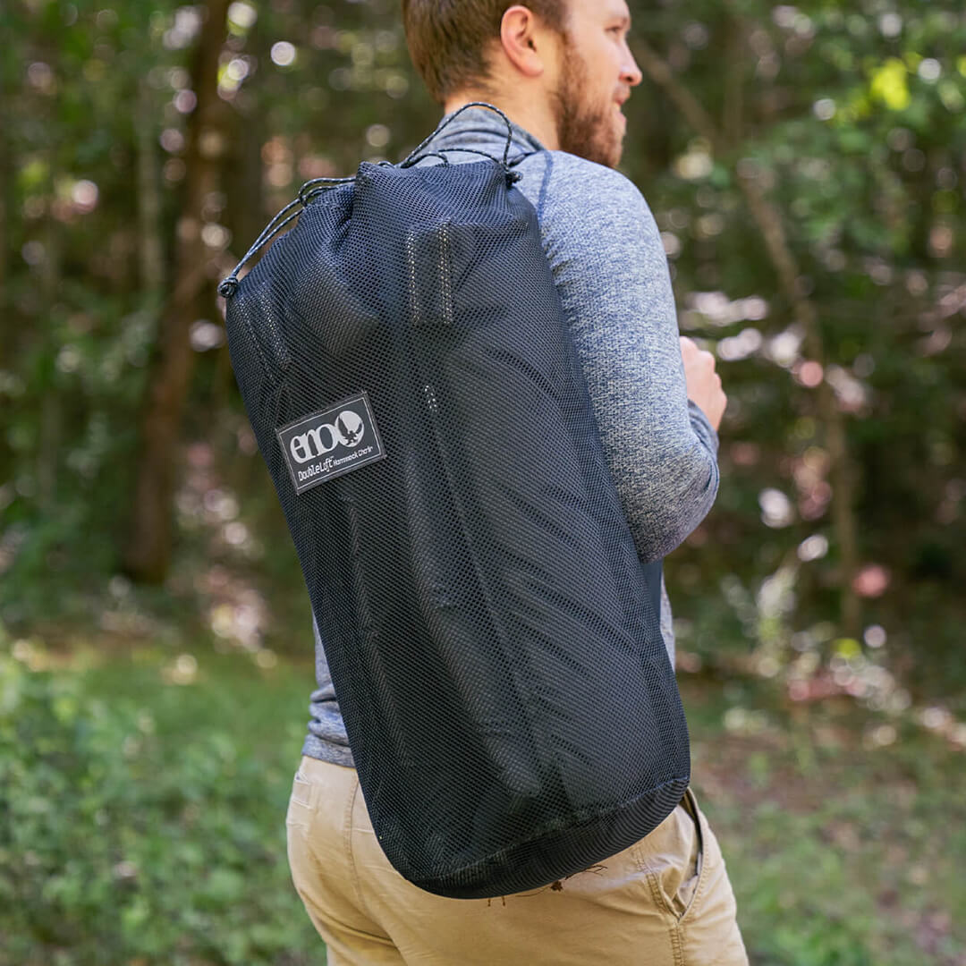 A person carrying a packed up DoubleLoft Hammock Chair with shoulder strap in a forest environment.