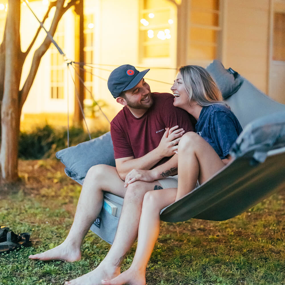 Smiling young couple looking at one another in front of home in an ENO backyard hammock.