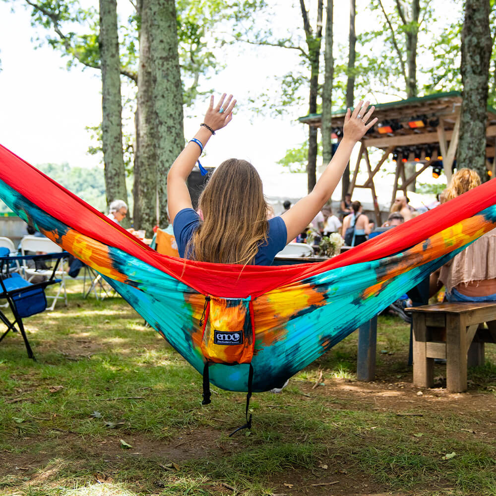 A woman sits in a DoubleNest Hammock Print in front of a stage with their hands raised in the air.