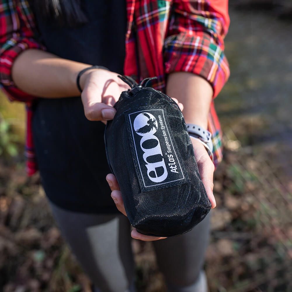 A young woman in a red flannel shirt holds a packed ENO Atlas Hammock Straps stuff sack in hands.