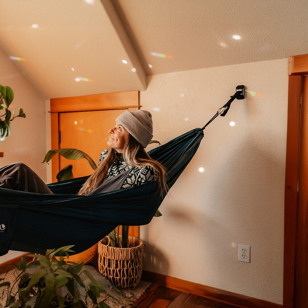 Person relaxing in a hammock indoors with plants around set up with the ENO Deluxe Hammock Hanging Kit.