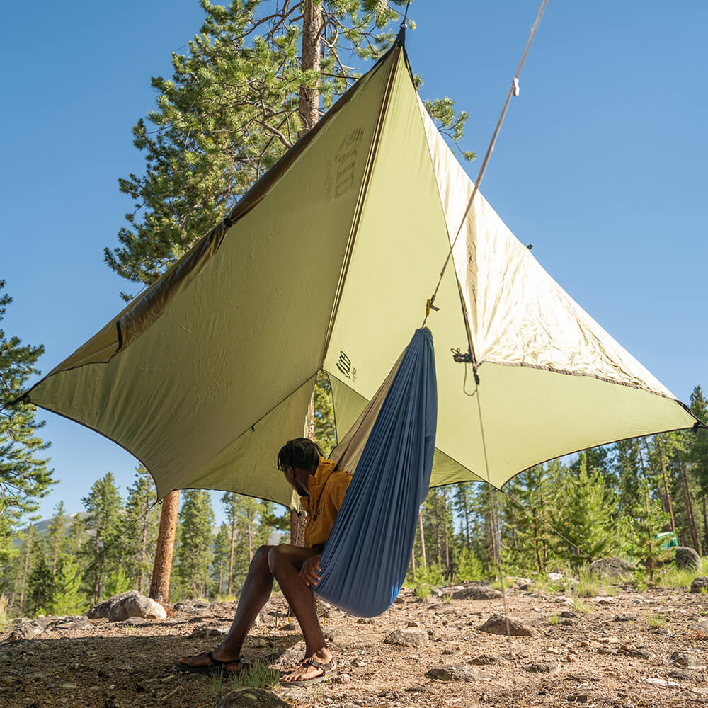 Person sitting under the ENO HouseFly Rain Tarp in a forested area