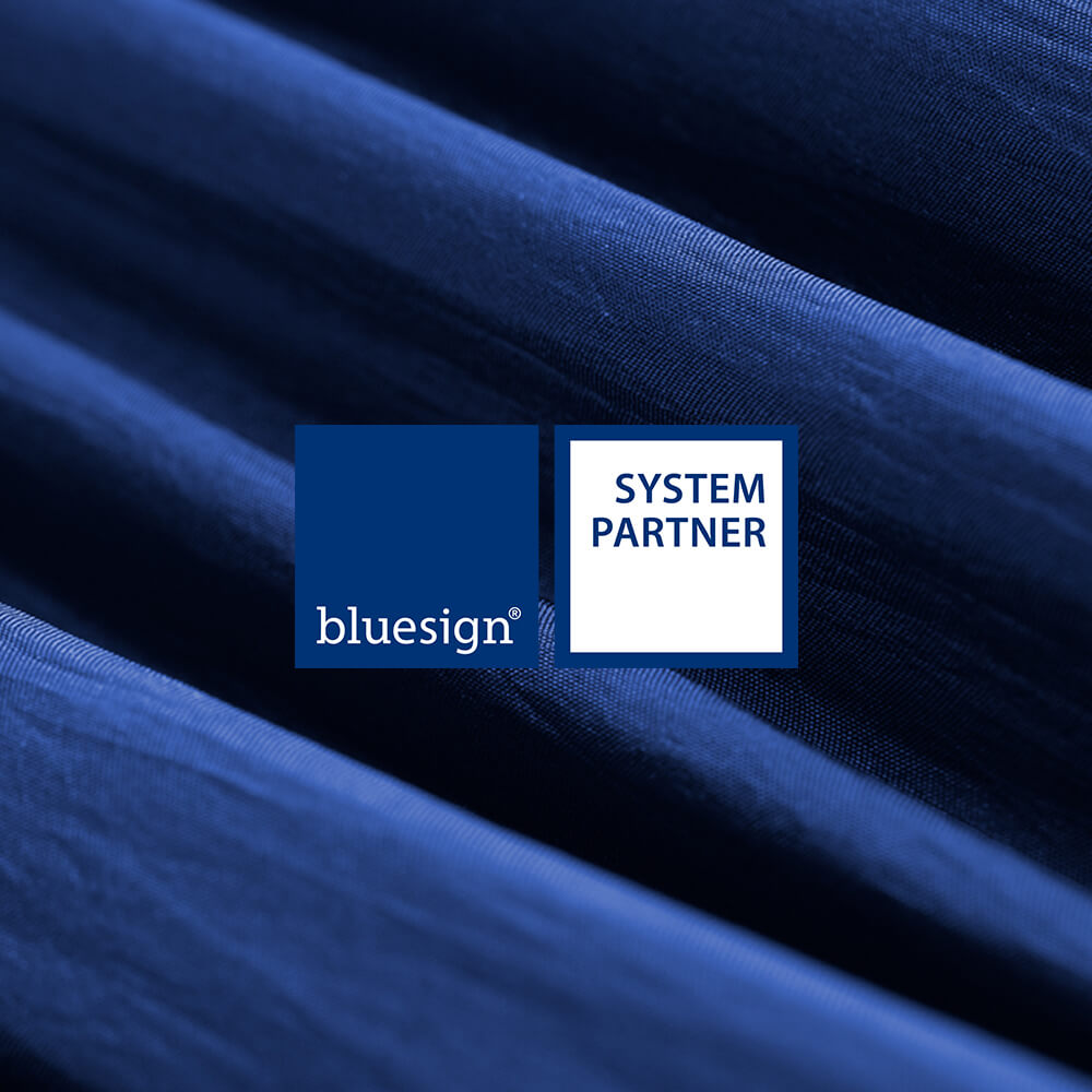 bluesign System Partner logo with detail of blue fabric in background.