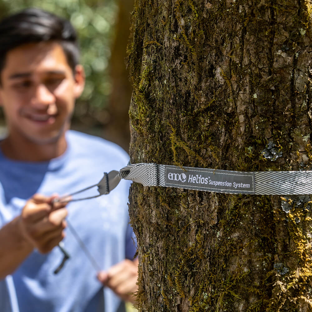 A person wrapping an ENO ultralight hammock strap around a tree and pulling snug.