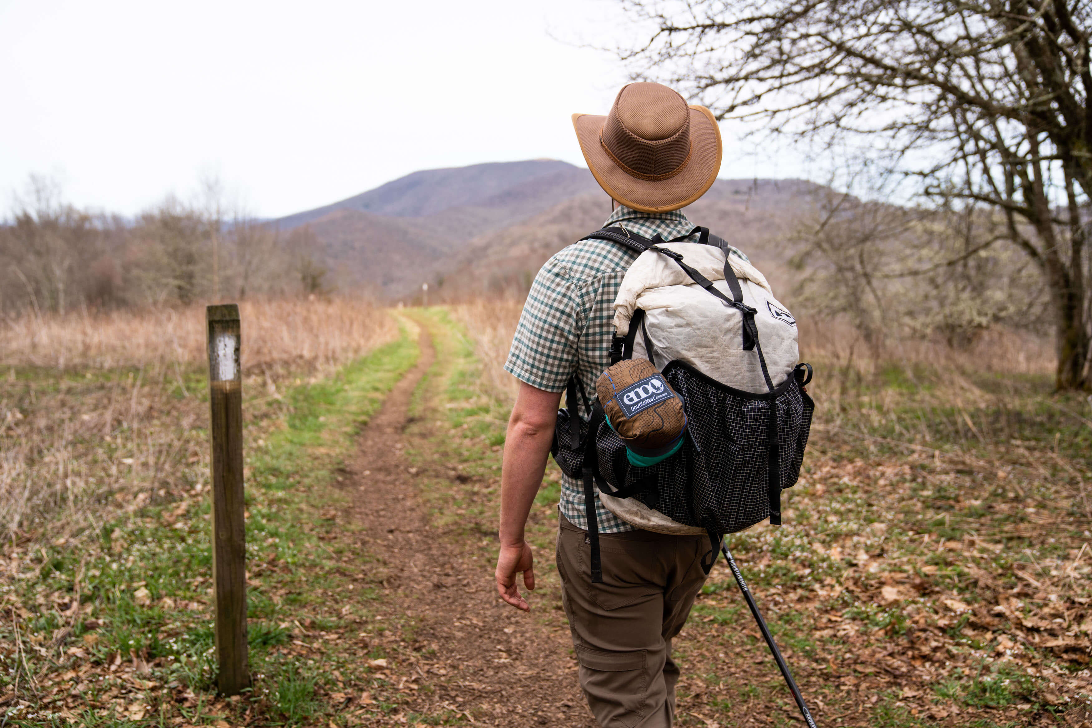 A man walking on a trail with hiking backpack and ENO hammock attached