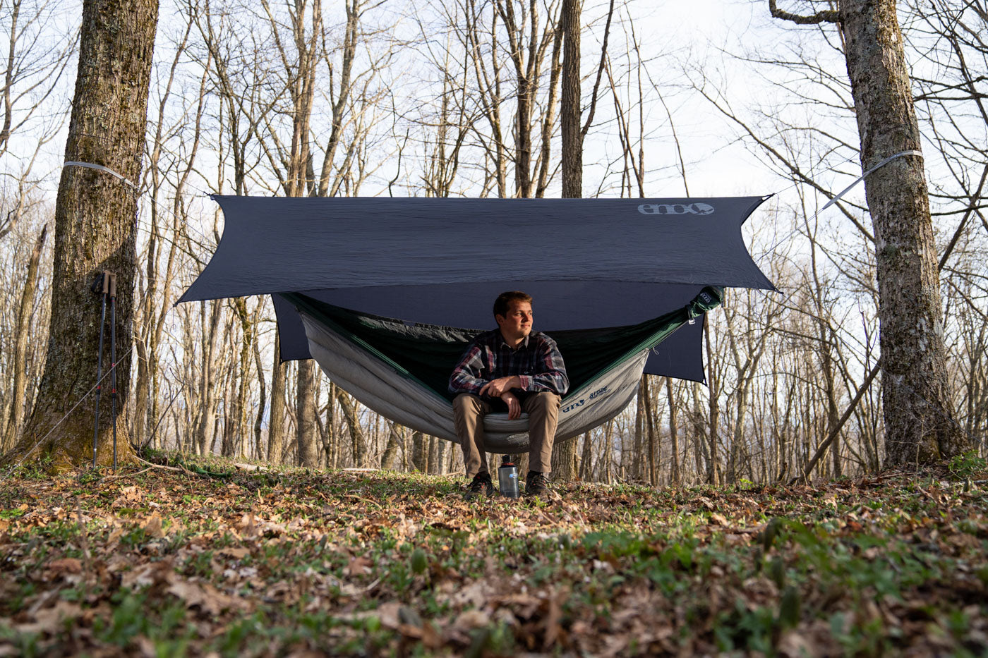 A man sits in his ENO hammock camping set up while looking off into the sun.