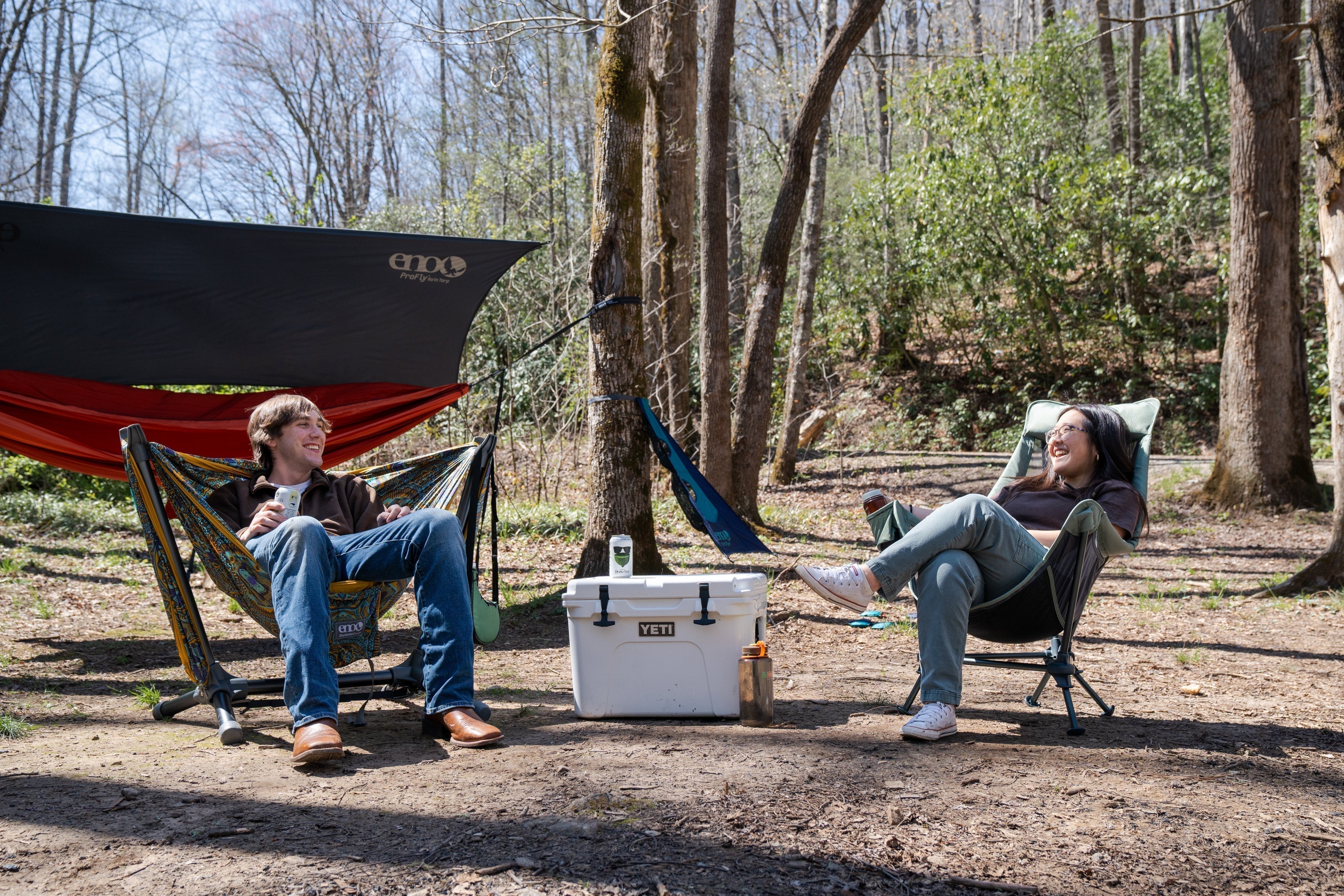 Kayla and her boyfriend sitting at a camp site in an ENO Parklite Hammock Chair Stand and an ENO Lounger DL Mesh Chair. 