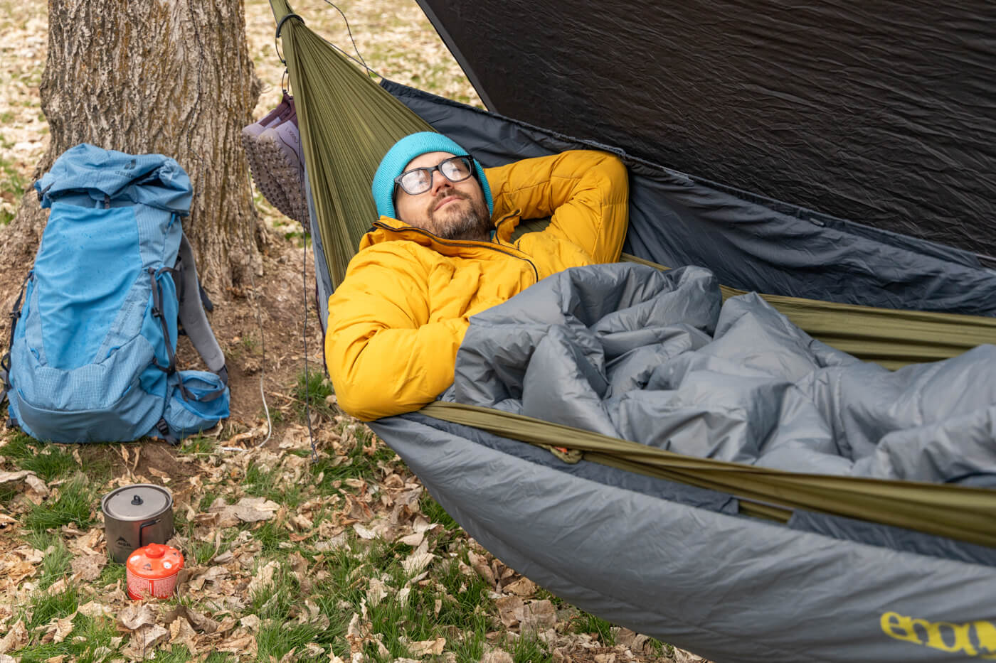 A man rests in his ENO SubLink Hammock Camping setup while backpacking in the woods