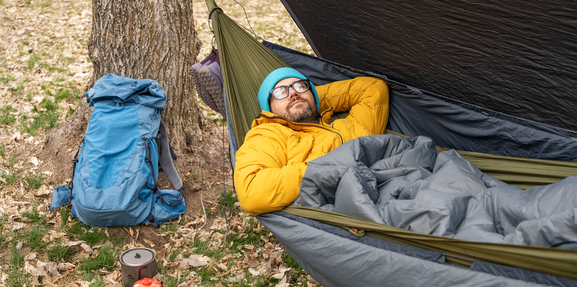 A man rests in his ENO SubLink Hammock Camping setup while backpacking in the woods