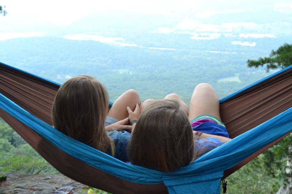 two girls sitting in a hammock overlooking a forest
