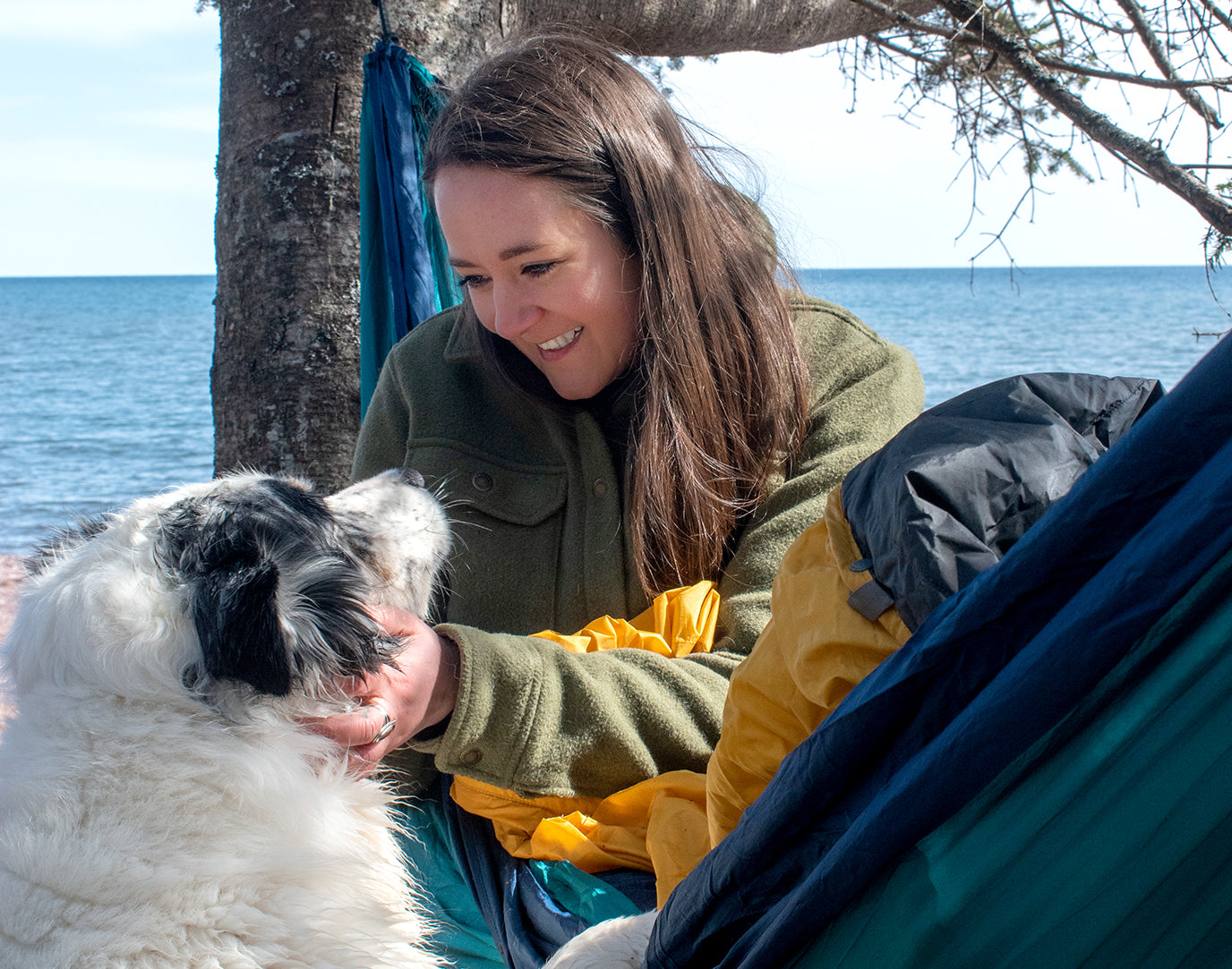 A woman pets her dog while sitting in an ENO SingleNest Hammock.