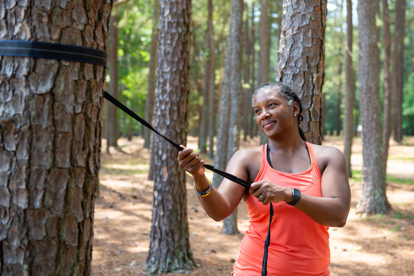 A woman is tightening ENO Hammock Straps onto a tree in the woods
