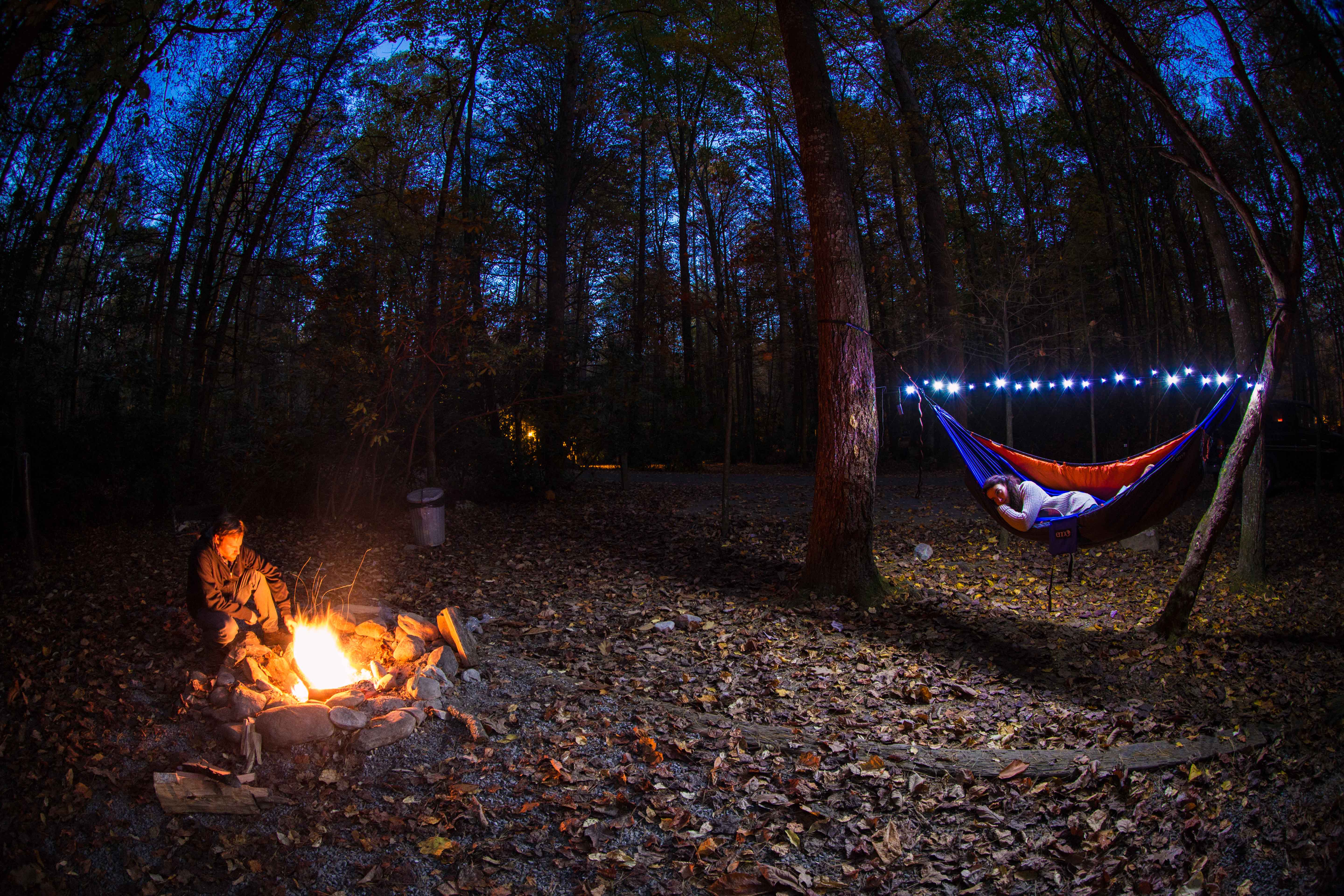 A girl in an ENO hammock with ENO Twilights above head watching a guy attend to a campfire