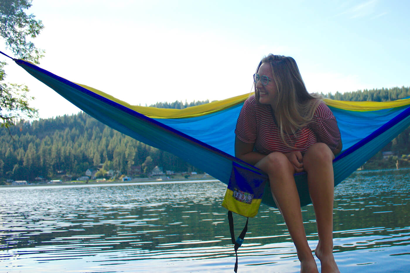 Lee Brewer is laughing in an ENO Hammock with a body of water behind her.
